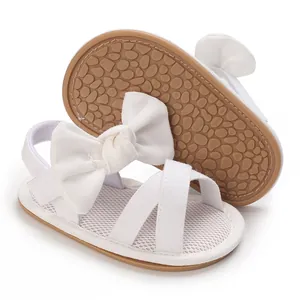 Detail view of white baby sandals featuring a soft rubber sole and elegant decorative bow