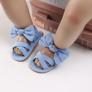 Detail shot of blue denim baby sandals with large bow decoration on doll feet.