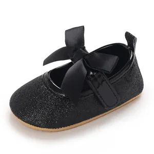 Close-up of black glittery baby girl princess shoes with a large satin bow detail