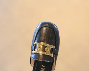 Detail von schwarzen Leder-Slippern für Mädchen mit goldener Kette und Prägestruktur