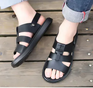 Detalle de sandalias de cuero negro para hombre con logo de libélula sobre madera.