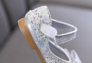 Primer plano de los zapatos de princesa plateados para niña con detalles de pedrería y perlas