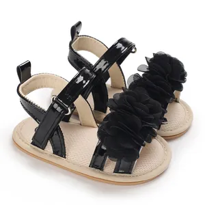 Gros plan de sandales noires pour bébé fille avec grandes fleurs en maille et brides vernies.