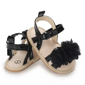 Détail de sandales d'été noires pour bébé fille avec une grande fleur décorative en tissu.