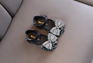 Detailansicht der glitzernden Strass-Schleife auf schwarzen Mädchen-Schuhen.