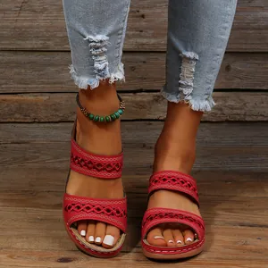 Détail de sandales compensées rouges ajourées pour femmes sur fond de bois brut.