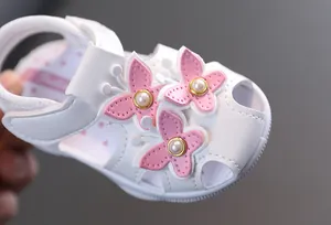 Détail d'une sandale blanche pour bébé avec des papillons roses et des perles centrales