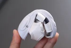 Gros plan d'une sandale pour bébé blanche montrant la semelle souple et flexible