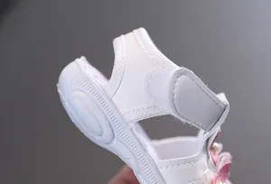 Gros plan d'une sandale blanche pour bébé fille avec une sangle velcro réglable.