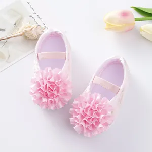Detailed view of pink infant princess shoes with large ruffled flower and soft sole.