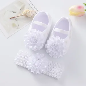 Gros plan de chaussures de princesse pour bébé blanches avec fleurs et bandeau assorti