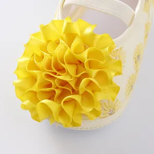 Close-up of a vibrant yellow ribbon flower detail on white soft-soled baby princess shoes