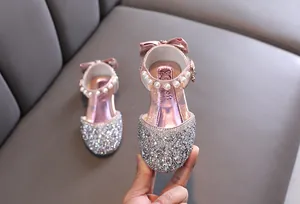 Primo piano di scarpe da principessa rosa scintillanti con catena di perle e fiocco.