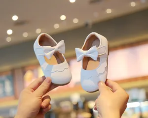 Nahaufnahme weißer Baby-Mädchen-Lederschuhe mit Schleife und weicher Sohle.