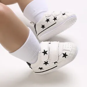 Close-up of white baby sneakers with black star patterns and hook and loop straps.