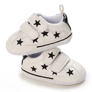 Detailed view of white baby sneakers with black star patterns and velcro straps.