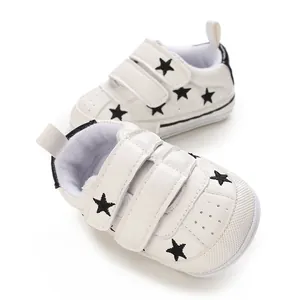 Close-up of white baby sneakers featuring black star patterns and hook and loop closure