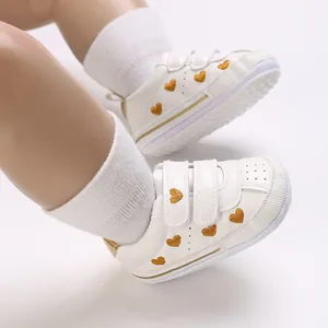 Detailed view of white baby sneakers featuring gold heart embroidery and velcro straps.