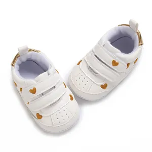 Detailed view of white baby sneakers featuring gold heart embroidery and triple Velcro straps