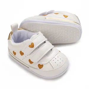Detail showing the white baby sneaker's non-slip sole and gold heart embroidery
