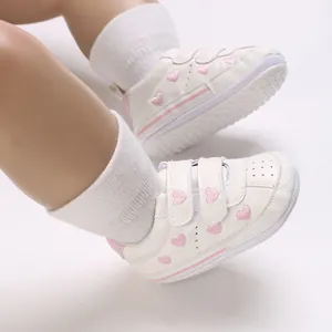 Vista ravvicinata di scarpe primi passi per neonati bianche con ricami di cuori rosa.