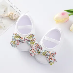 Detailed view of white baby princess shoes with colorful floral bows and soft soles