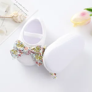 Top and sole view of white baby princess shoes with a colorful floral bow
