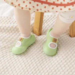 Detail view of light green baby walker shoes with soft non-slip soles on a rug