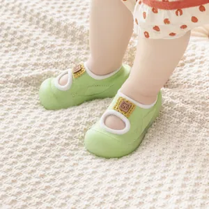 Close-up of green baby walking shoe socks on a soft knit blanket background.