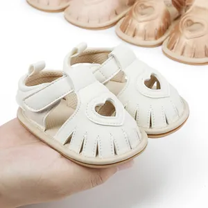 Detailed view of white baby summer sandals with heart cutout being held in hand