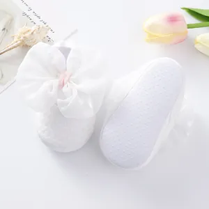 Detail of white baby walking shoes with soft non-slip sole and large silk bow