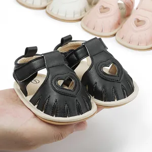 Close-up detail of black leather baby sandals with heart cutouts and fringe toe