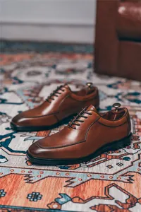 Zapatos Oxford clásicos de cuero marrón sobre una alfombra con motivos en casa
