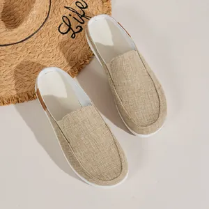 Nahaufnahme beiger Canvas-Mules für Damen mit sommerlichem Strohhut im Hintergrund