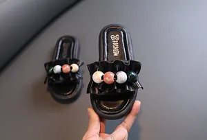 Detail of girls' black sandals with colorful beads and ruffle straps on thick sole.