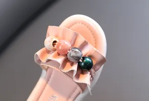 Close-up of pink girl's sandals featuring elegant ruffles and colorful decorative beads.