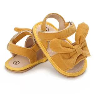 Close-up of yellow corduroy baby sandals featuring a decorative bow and velcro strap.