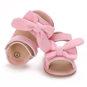 Detail of pink corduroy baby sandals with large bow decoration for infant girls.