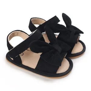 Close-up detail of black corduroy baby girl sandals with large decorative bow on white background