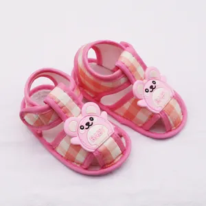 Primer plano de sandalias rosas para bebé con cuadros y un tierno oso con la palabra BABY