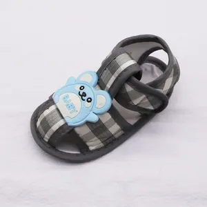 Detalle de sandalia de verano para bebé con suela blanda, cuadro escocés y oso azul.