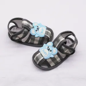 Primer plano de sandalias para bebé a cuadros con osito azul y suela blanda.