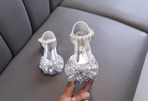Detalle de zapatos de princesa plateados para niña con lazo brillante y tira de perlas