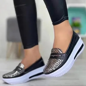 Primer plano de mocasines negros de plataforma para mujer con detalle de piel de serpiente.