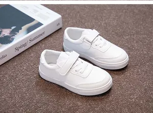 Close-up of classic white children's sneakers with velcro straps on textured brown surface.