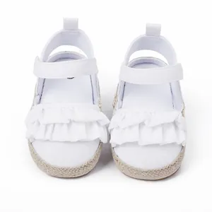 Vista detallada de los zapatos blancos para bebé con bonitos volantes y suela trenzada.