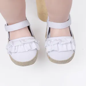 Primer plano de zapatos de bebé blancos con detalles de volantes y suelas trenzadas