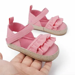 Detalle de sandalias rosas para bebé con volantes, cierre de velcro y suela de yute