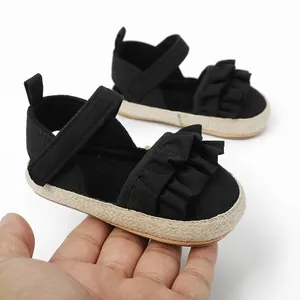 Primer plano de sandalias negras para bebé con volantes, velcro y suela tejida