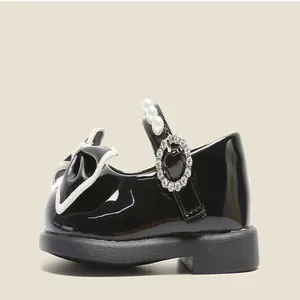 Side detail of girls' black patent leather Mary Jane shoes with pearl strap.